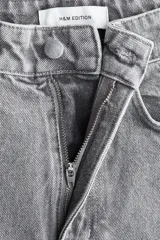 Jean de tiro alto, corte ancho y pierna recta, confeccionado en denim de algodón rígido color gris lavado. Presenta una franja lateral negra contrastante con acabado desflecado en los bordes.