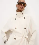 Trench coat Cortelle de gabardina de viscosa color beige, con diseño largo, mangas largas, cuello alto con solapas y cierre cruzado con botones carey. Incluye tira para anudar en la cintura y bolsillos laterales.