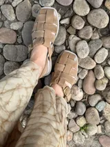 Sandalias de cuero negro con diseño de tiras entrelazadas, estilo huarache, con pulsera ajustable al tobillo mediante hebilla metálica.