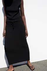 Falda midi de tiro medio en color negro, confeccionada en tejido de punto con textura y cintura elástica ajustable con cordones.