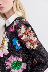 Saco corto de lentejuelas negras con bordados florales multicolores hechos a mano. Presenta cuello redondo, mangas largas y cierre frontal con ganchos invisibles.
