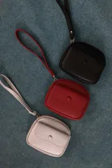 Monedero compacto de símil cuero con textura granulada, cuenta con un compartimento principal con cierre, correa de mano y un bolsillo frontal con solapa y botón a presión.