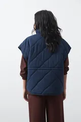 Chaleco acolchado de nylon con diseño capitoneado, cuello alto y cierre frontal con botones a presión. Presenta un calce amplio y versátil.