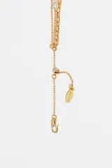 Collar de triple capa en tono dorado con cierre de mosquetón y largo regulable. Presenta una cadena interior con dijes de corazones en cristales de diversos colores (verde, rosado, celeste, amarillo y negro) y dos cadenas adicionales con pequeñas perlas blancas intercaladas.