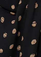 Blusa de viscosa con cuello alto drapeado y mangas cortas. Presenta un diseño recto con estampado de topos en tonos contrastantes sobre fondo negro.