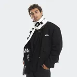 Bufanda tejida en color negro con detalles en blanco, presenta un diseño con estampado de globos terráqueos y patrones de damero. Cuenta con flecos en los extremos.