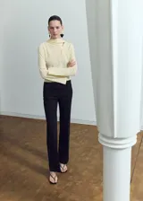 Blusa de manga larga en color crema, confeccionada en poliéster. Presenta un diseño de cuello alto con un sutil detalle de abertura frontal y corte recto.