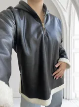 Buzo negro de ecocuero con capucha, cierre dorado a mitad del torso y puños y ruedo con forro de piel sintética blanca.