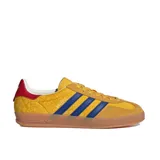 Championes Adidas Gazelle Indoor con exterior de gamuza amarilla y estampado geométrico sutil. Presenta las tres tiras laterales en azul, detalle en el talón en color rojo y suela de caucho color caramelo.
