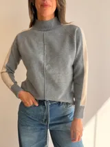 Sweater de tejido de punto en color beige con cuello alto y costura central vertical. Presenta mangas ranglan con una franja lateral en color marrón oscuro que genera contraste, y terminaciones en tejido acanalado en puños y ruedo.