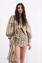 Minifalda de tafeta con diseño de rayas verticales en tonos bronce y beige. Presenta un estilo drapeado con un lazo lateral largo y caída fluida.