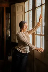 Blusa de muselina de algodón color beige, con diseño totalmente fruncido, cuello alto, mangas largas y terminaciones con volados en cuello, puños y ruedo.