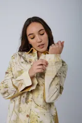 Chaqueta color beige con estampado abstracto en tonos amarillos, con cuello camisero, cierre frontal con botones, bolsillos plaqué y puños camiseros.