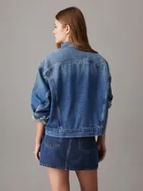 Campera de denim azul medio vintage, corte relaxed boxy, confeccionada con 20% de algodón reciclado. Tiene cuello en punta, bolsillos de parche en el pecho, bolsillos de hendidura en la cintura, botones metálicos de la marca y parche con logo de Calvin Klein en el bolsillo del pecho.
