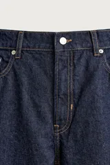 Pantalón de jean corte slim fit, color azul oscuro, con diseño de cinco bolsillos, tiro medio y cierre frontal con cremallera y botón.