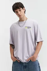 Remera oversize color marrón claro con estampado gráfico en la espalda que incluye frases como "Stay Original Forever", "All About Having Fun" y el logo de Mistral, junto con otros garabatos y stickers.