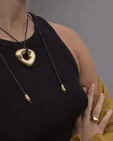 Collar con dije de forma irregular en tonos dorados y plateados, suspendido de un cordón doble de algodón negro.