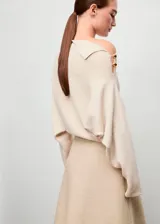 Jersey de punto color beige, con cuello asimétrico y detalle de botones efecto joya en el hombro, de manga larga y diseño recto.