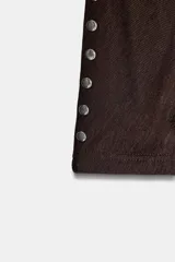 Camiseta de cuello barco y manga larga tipo murciélago, confeccionada en tejido de punto gris melange. Presenta detalle de tachas metálicas a lo largo de los hombros y las mangas.