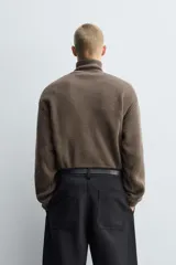 Jersey de punto de corte relajado, color marrón, con cuello perkins y cierre frontal de cremallera. Presenta manga larga y acabados en rib en puños y bajo.