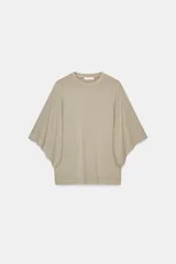 Camiseta oversize de manga corta tipo capa, color beige claro con efecto lavado. Presenta cuello redondo y dobladillos en las mangas y el bajo.