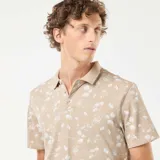 Remera polo de piqué color beige con estampado de palmeras y motivos playeros en blanco.