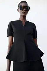 Top peplum confeccionado en hilatura de algodón de color bordó, con escote en V pronunciado, mangas cortas abullonadas y bajo con vuelo.