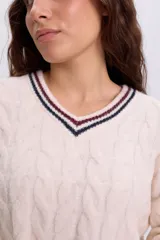 Buzo tejido de punto color crudo, con cuello redondo, puños y ruedo acanalados con rayas en contraste. Presenta un diseño trenzado en la trama y un gran número '96' aplicado en la espalda.