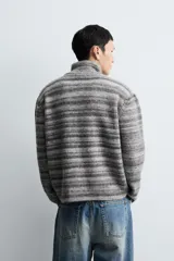 Chaqueta de punto con diseño de rayas horizontales en tonos grises, cuello subido y cierre frontal de cremallera completa. Presenta un corte relajado y acabados en rib en puños y bajo.