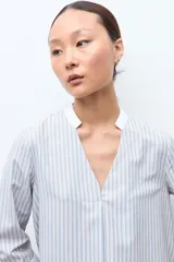 Blusa rayada en tonos beige y celeste, con cuello mao, escote en V y mangas 3/4 con puños blancos.