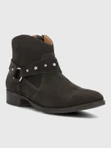 Bota corta de gamuza color marrón oscuro, con diseño de correa decorativa con tachas metálicas y hebilla lateral. Cuenta con cierre lateral para un ajuste cómodo y suela de goma.