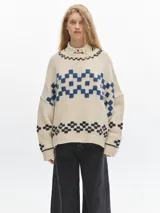Sweater de lana color crema con diseño geométrico en azul y negro. Tiene cuello redondo y corte holgado.