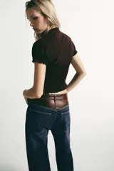 Top marrón de tejido texturizado con cuello redondo, lazada frontal y escote en pico. Presenta mangas cortas abullonadas con terminación elástica, cuerpo con estructura tipo nido de abeja y cierre frontal con botones.