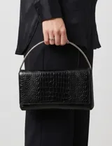 Cartera tipo clutch de cuero sintético negro con textura croco brillante y solapa frontal, con asa superior metálica arqueada en acabado plateado.