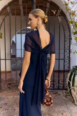 Vestido largo azul marino sin mangas, de corte recto con tajo lateral y diseño strapless con sobrecapa fluida superpuesta.