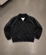 Campera deportiva de corte boxy en color negro, con diseño de cuello camisero, mangas raglán con vivos blancos y estampado circular con las siglas BHN en la espalda.
