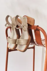 Sandalias de cuero color beige con punta cuadrada, plataforma baja y taco bloque de madera. Presentan tiras finas en el empeine y pulsera ajustable con hebilla metálica en el tobillo.