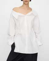 Camisa blanca de algodón con diseño desestructurado, escote asimétrico que deja un hombro al descubierto, manga larga y botonadura frontal.