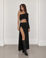 Vestido largo negro de corte asimétrico con una sola manga larga, abertura lateral en la cintura y tajo pronunciado en la falda.