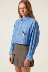 Camisa corta celeste a rayas blancas con bordes sin rematar, bolsillos de parche con solapa y pines removibles con motivos de Jamaica.