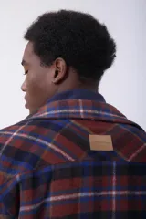 Sobrecamisa de corte holgado con diseño a cuadros en tonos beige y marrón, confeccionada en tejido de textura suave. Presenta cuello clásico, cierre frontal con botones, dos bolsillos con solapa en el pecho y puños abotonados.