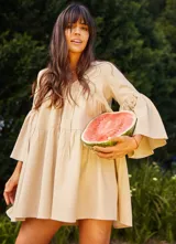 Vestido corto color beige, de lino y corte en A, con escote en V con tiras para anudar y mangas amplias.