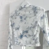 Top de microtul blanco con estampado tie-dye en tonos celeste y gris, cuello alto y mangas largas.