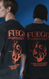 Remera de manga corta con cuello redondo y calce oversize, color negro con efecto nevado. Presenta una estampa frontal en color naranja con diseño gráfico de un rostro rodeado de llamas y texto tipográfico.