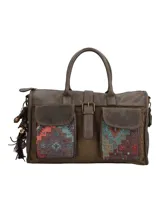 Cartera de mano marrón de estilo bohemio con detalles en tela étnica tipo tapicería bajo los bolsillos frontales con solapa. Cuenta con doble asa fija, correa ajustable y desmontable, cierre superior y llavero colgante con borla y cuentas decorativas.