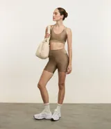 Top deportivo color tostado, confeccionado en microfibra con efecto satinado. Presenta copas y correas dobles ajustables.