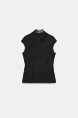 Top negro confeccionado en tejido elástico, con cuello perkins y mangas muy corta. Presenta un detalle de aplique de encaje a tono que cruza desde el cuello hasta el lateral de la prenda.