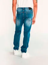 Jeans de corte slim en denim azul con efecto lavado, diseño de cinco bolsillos, cierre de cremallera y botón metálico con logo de la marca.