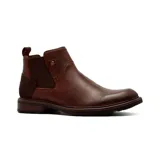 Bota tipo Chelsea de cuero color marrón, con paneles laterales elásticos, detalle de remache metálico y refuerzo de gamuza en el talón. Cuenta con suela de goma con textura y tirador trasero.