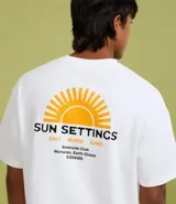 Remera de algodón blanca, corte relajado (relaxed fit), con cuello redondo y manga corta. Presenta un pequeño estampado frontal en el pecho con un sol estilizado y el texto "Sun Settings".